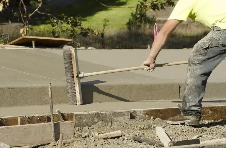 A worker using broom to finish the concrete surface